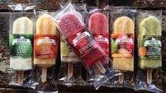 four popsicles are wrapped in plastic and sitting on a wooden surface, each with different flavors