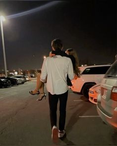 a man and woman are walking in the parking lot at night with their arms around each other