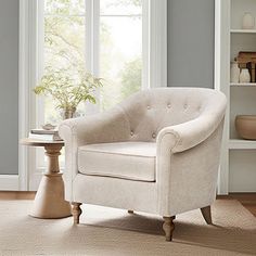 a white chair sitting in front of a window next to a table with a potted plant on it