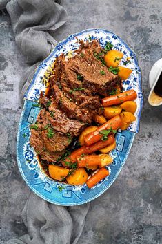 a blue and white plate topped with meat and carrots next to a cup of coffee