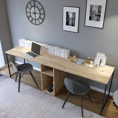 a wooden desk with two chairs and a clock on the wall behind it in a room