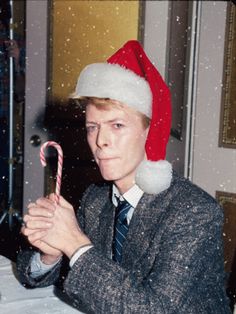 a man wearing a santa hat holding a candy cane in front of his face while sitting at a table