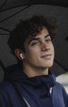 a young man with curly hair holding an umbrella