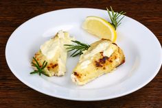 two pieces of chicken on a white plate with lemon wedges