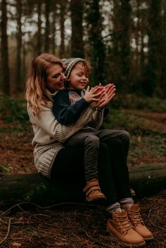 a mother and her child are sitting on a log in the woods with their hands together