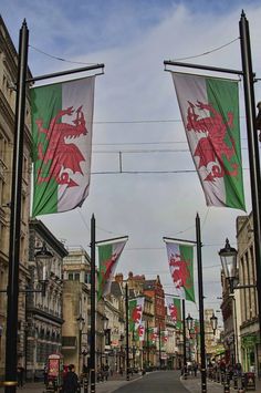 several flags are flying in the air on a city street with old buildings and cobblestone streets