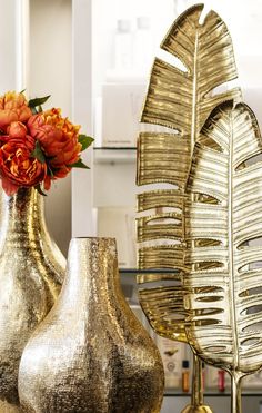 three gold vases with flowers in them sitting on a table next to each other