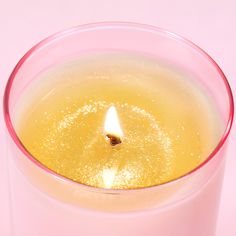 a lit candle in a clear glass on a pink background