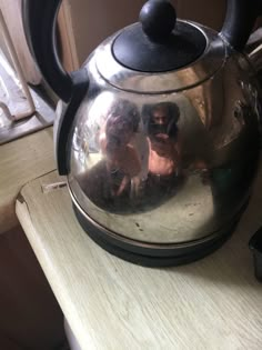 a tea kettle with two people reflected in it