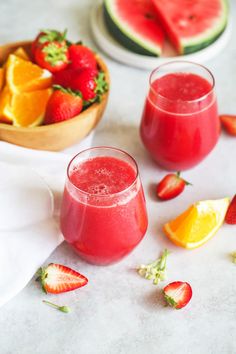 two glasses of watermelon juice with strawberries and oranges in the background