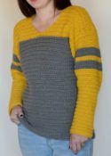 a woman standing in front of a white wall wearing a yellow and gray sweater with striped sleeves