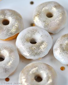 four donuts with white frosting and gold sprinkles on a plate