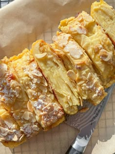 a pastry with almonds and powdered sugar sits on a napkin next to a knife