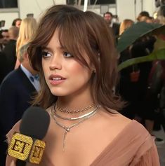 a woman in a pink dress is holding a microphone and talking to someone on the red carpet