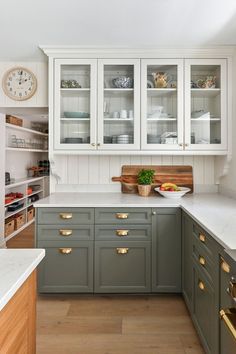 a kitchen with green cabinets and white counter tops, gold pulls on the cupboards