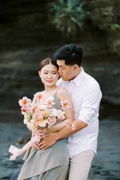 a man and woman standing next to each other on a riverbank holding bouquets