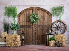 hay bales and plants are arranged in front of an old wooden door with a wagon wheel