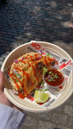 a person holding a plate with food on it and dipping sauce in the other hand