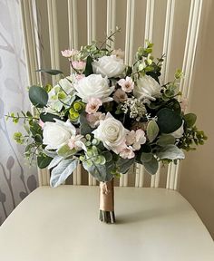 a bouquet of flowers sitting on top of a white table next to a wall with vertical blinds