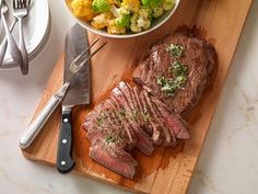 a wooden cutting board topped with meat and veggies next to a bowl of broccoli