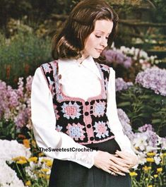 a woman standing in front of flowers wearing a crochet top and black skirt