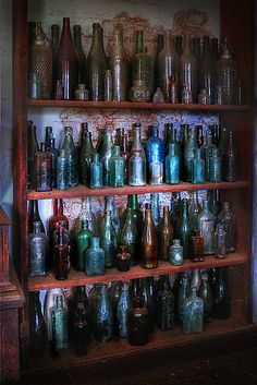 an old wooden shelf filled with lots of different colored glass bottles on it's sides