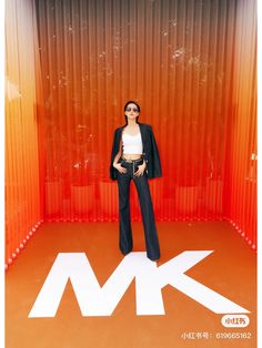 a woman standing in front of an orange and white wall with the letter k on it