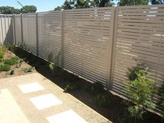 a white fence in the middle of a yard with trees and plants on either side