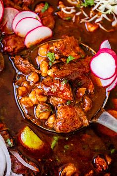 a spoon full of stew with meat and vegetables in it on top of a table