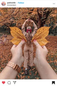 a person holding up a yellow leaf in front of a tree