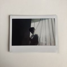 a polaroid photograph of a woman sitting in front of a window with white curtains