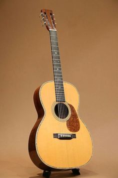 an acoustic guitar sitting on top of a wooden stand in front of a brown background