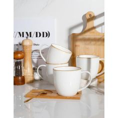 four white coffee cups sitting on top of a wooden board next to a cutting board