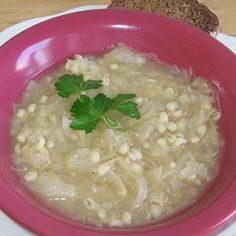 a pink bowl filled with soup and garnished with parsley next to a slice of bread