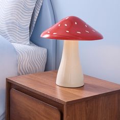 a red mushroom lamp sitting on top of a wooden night stand