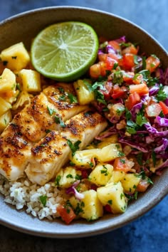 a bowl filled with fish, pineapples and rice next to a lime wedge