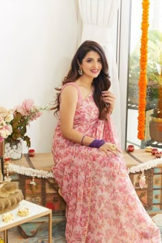 a woman in a pink dress sitting on a table next to a vase with flowers