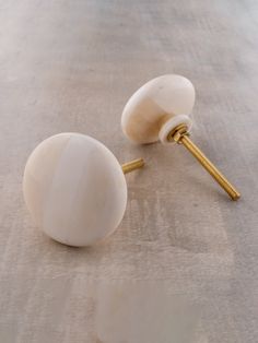 two white knobs with gold screws on top of a gray surface, next to each other