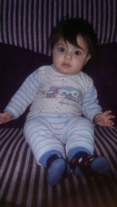 a small child sitting on top of a bed wearing blue and white striped pajamas with black socks