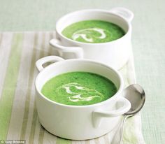 two white bowls filled with green soup on top of a striped table cloth next to a spoon