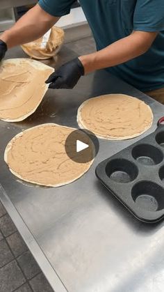 a man in blue shirt and black gloves making pizzas on top of a metal counter