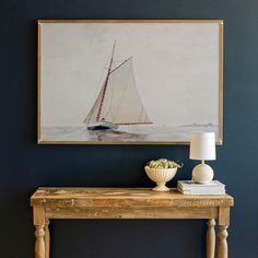 a painting hanging on the wall above a table with a vase and lamp next to it