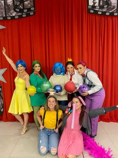 a group of people posing for a photo in front of a red curtain with balloons and wigs