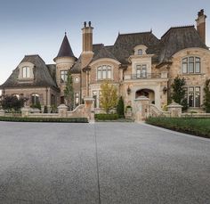 a large house that is in the middle of a driveway with hedges on both sides