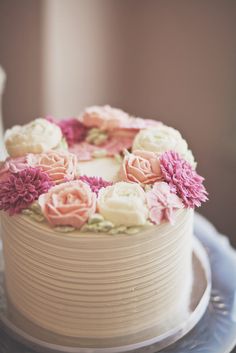 a white cake with pink and white flowers sitting on top of a blue platter