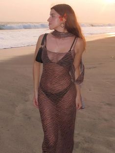 a woman standing on top of a sandy beach next to the ocean wearing a sheer dress