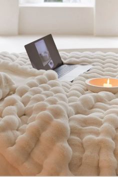 an open laptop computer sitting on top of a bed with a fluffy blanket around it