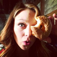 a woman holding a doughnut up to her eye and making a face with it