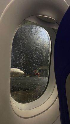 an airplane window with rain drops on it and another plane in the back ground behind it