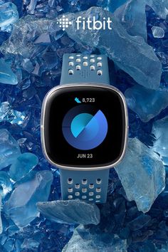 a smart watch sitting on top of blue glass pieces with the words fitbit above it